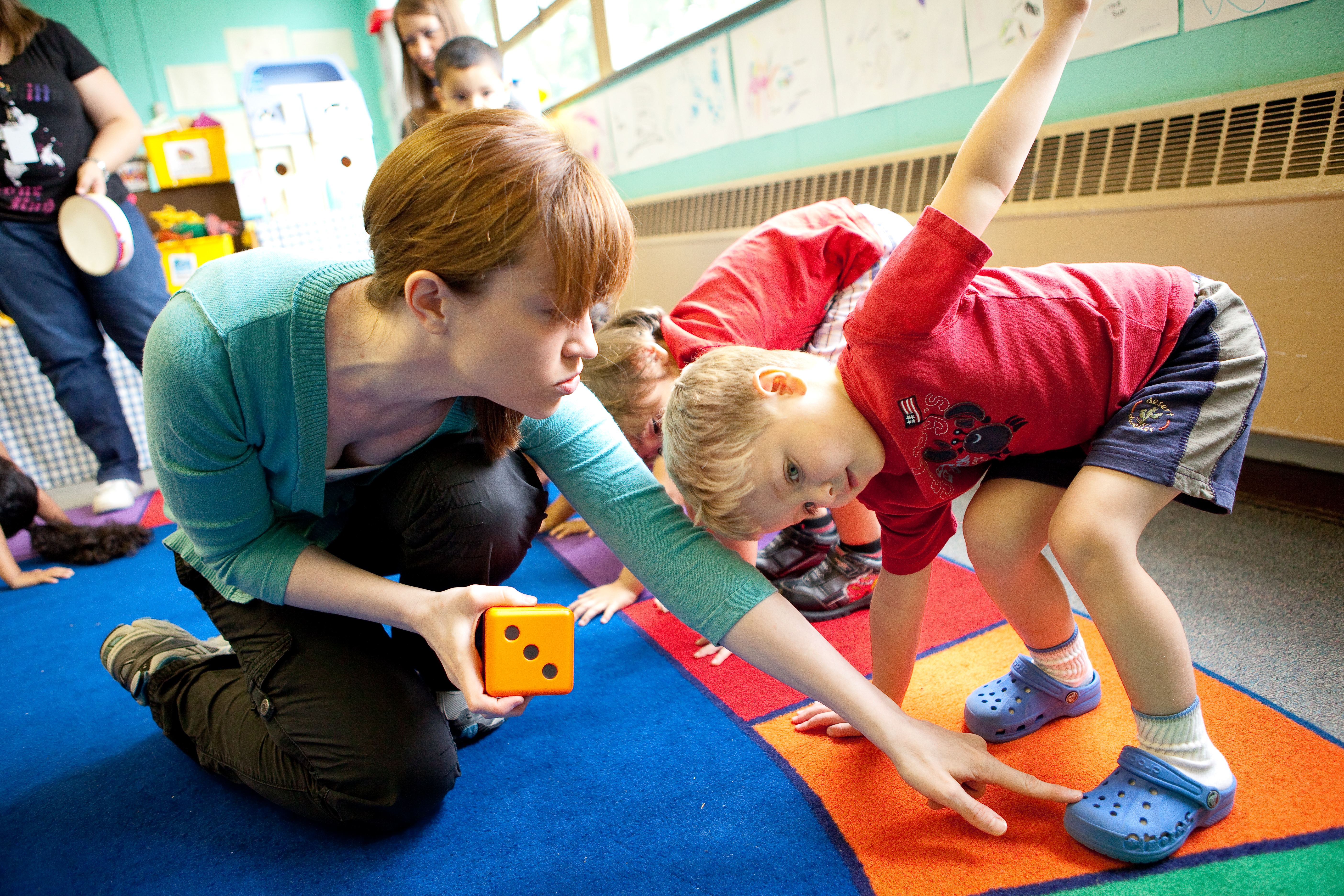 a teacher is showing a classroom of children a learning game on a colorful carpet