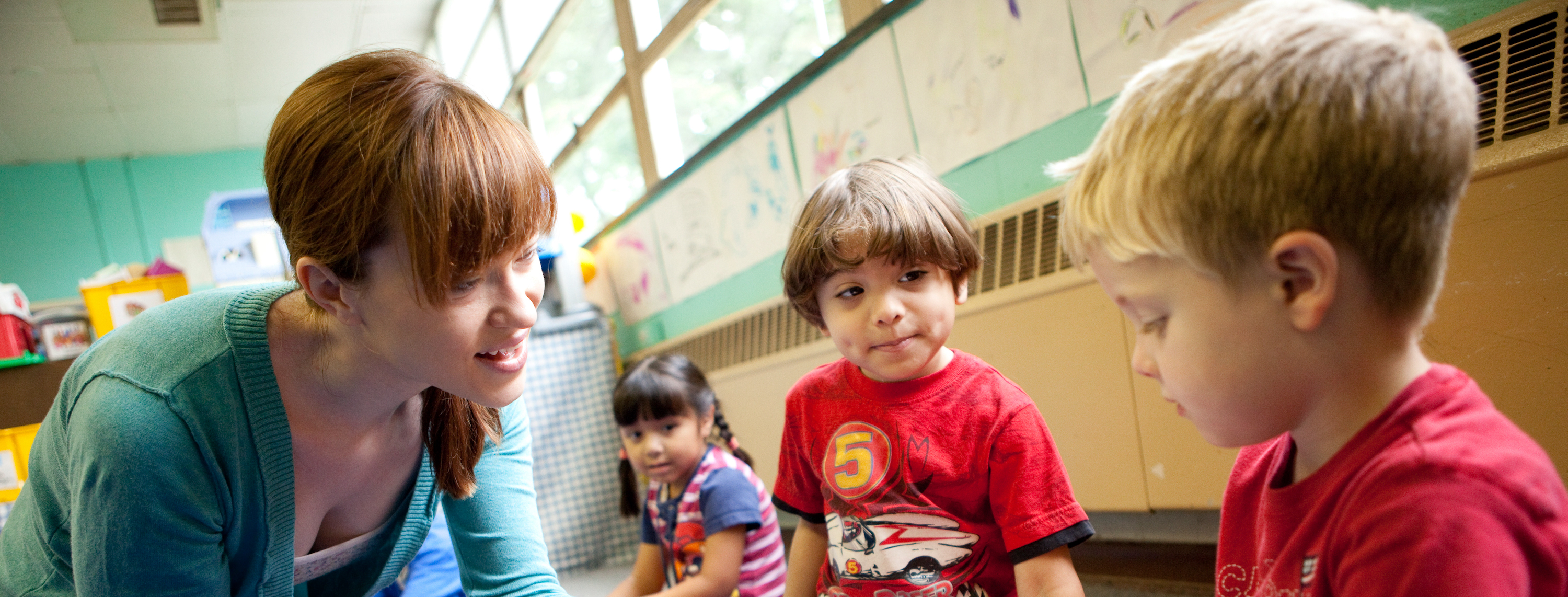 a teacher is showing children how to play a small drum in the middle of a colorful classroom