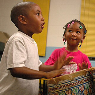 Photo of two young children playing a drum 