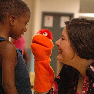 Photo of a student and teacher interacting with a puppet