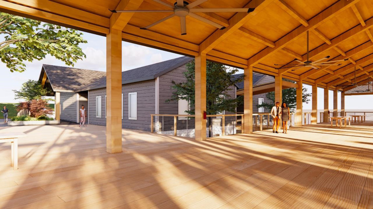Rendering of a covered wooden pavilion with ceiling fans and open sides, connected to a modern gray building with large windows and surrounded by trees.
