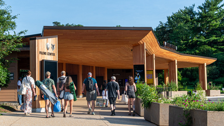 Group approaching Filene Center entrance with wooden canopy and surrounding greenery.