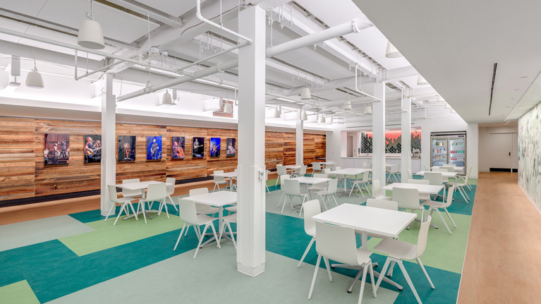 Bright, modern lounge with white tables and chairs, colorful flooring, and a wood-paneled wall displaying framed photos of past Wolf Trap performances.