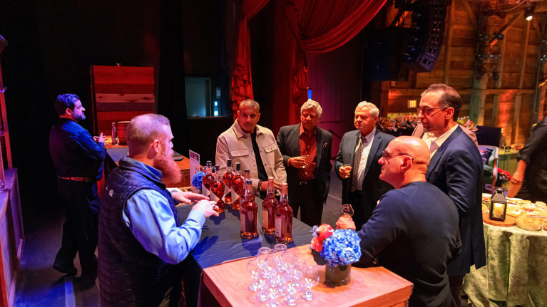 Group of people tasting drinks and chatting at a bar on stage at The Barns at Wolf Trap.