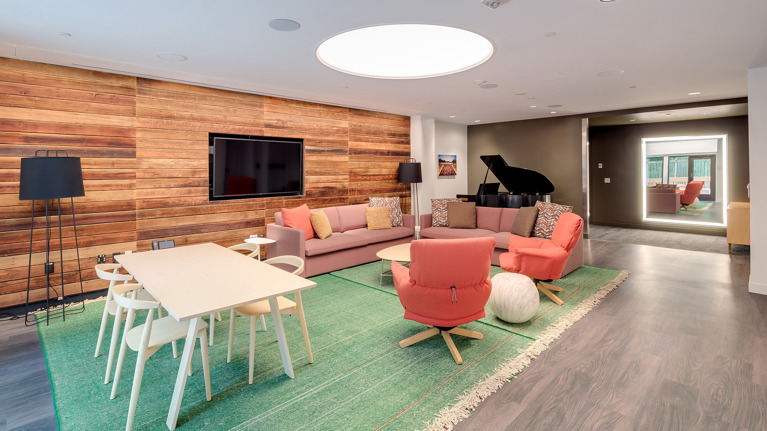 Spacious dressing room with lighted mirrors, white counters, seating areas with sofas, and a baby grand piano.