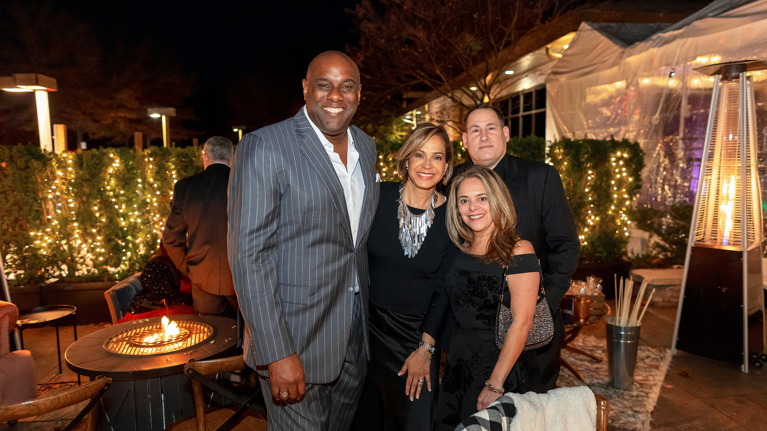 Group photo of four people standing outdoors at night in front of festive lights.