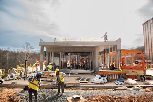 Construction workers in safety vests and helmets working on a partially built concrete structure with exposed framing and equipment on site.