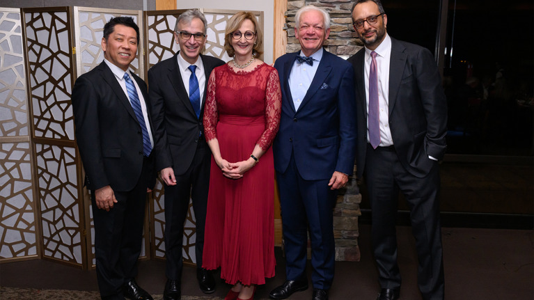 Five guests posing together in evening wear, including a red gown and dark suits.