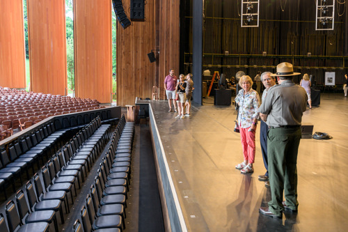 Visitors standing on stage during a backstage tour, looking out toward rows of theater seating.