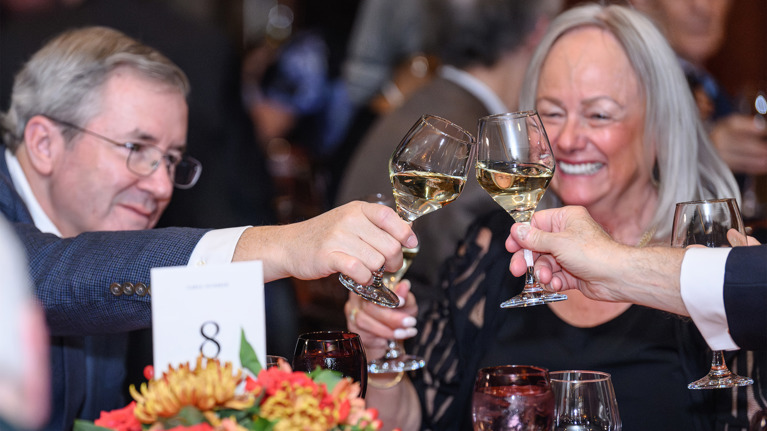 Close-up of guests clinking wine glasses in a toast over a decorated table.