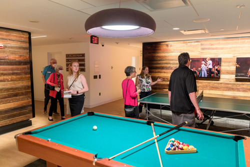 Guests in a renovated game room with a pool table and ping pong table, wood accent walls, and framed performance photos.