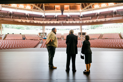Three people standing on stage facing the empty theater seating area with a view of the auditorium.