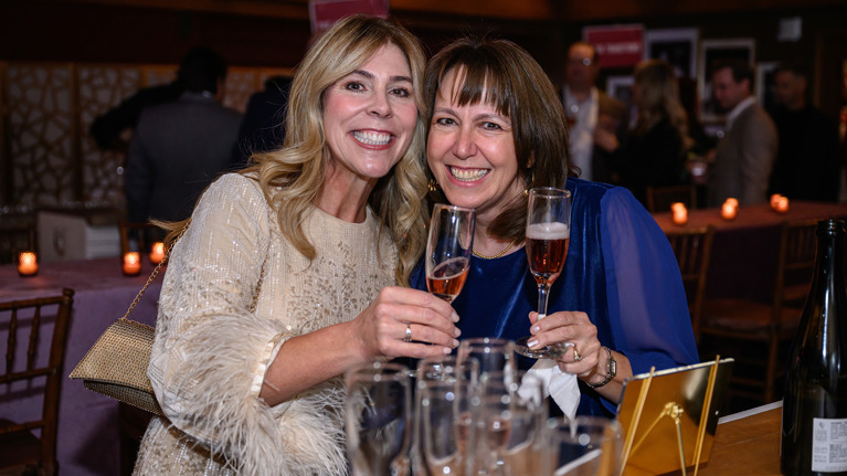 Two guests clinking glasses of sparkling wine at a table with multiple champagne flutes.