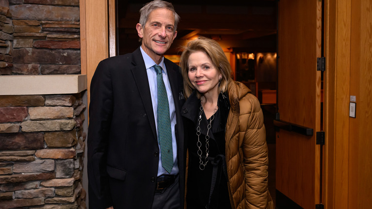 Two guests standing in front of a stone fireplace, dressed in formal attire.