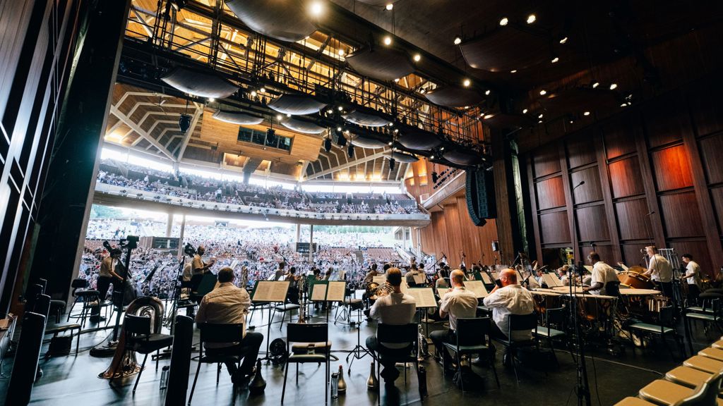 A stage view of an orchestra performance at the Filene Center, with a full audience on the lawn.