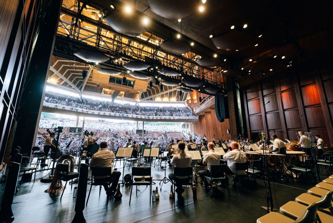 A stage view of an orchestra performance at the Filene Center, with a full audience on the lawn.