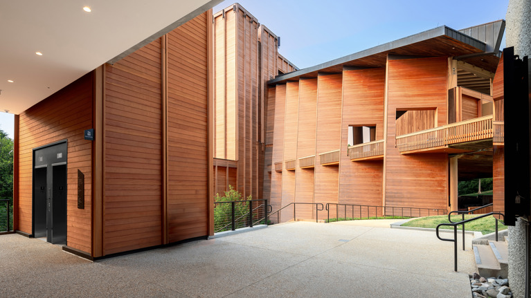 Accessible elevator area with wood-paneled walls and wide paved walkway near Meadow Commons.