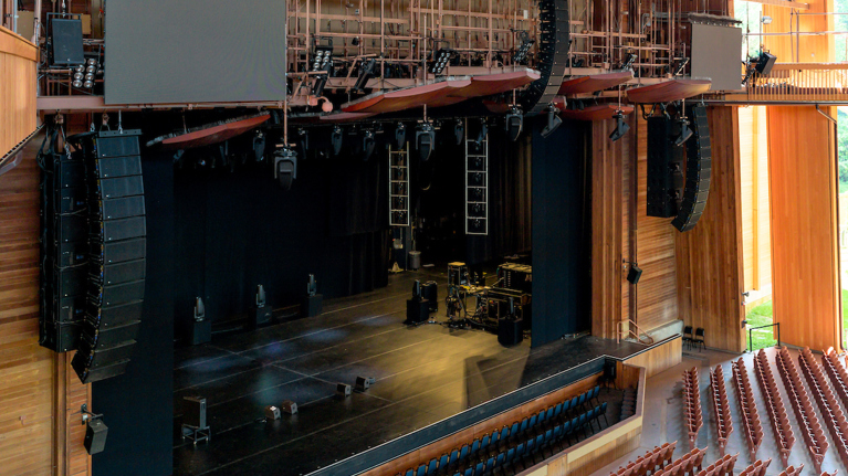 Angled view of stage showing upgraded sound system with multiple hanging speakers and lighting rigs.
