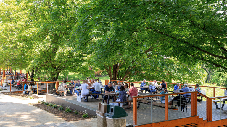 Large accessible picnic terrace with multiple tables, surrounded by trees and landscaped walkway.
