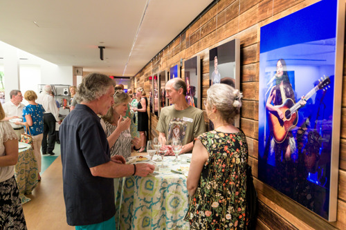 Guests gathered around cocktail tables in a reception area with wood-paneled walls and large performance photos.
