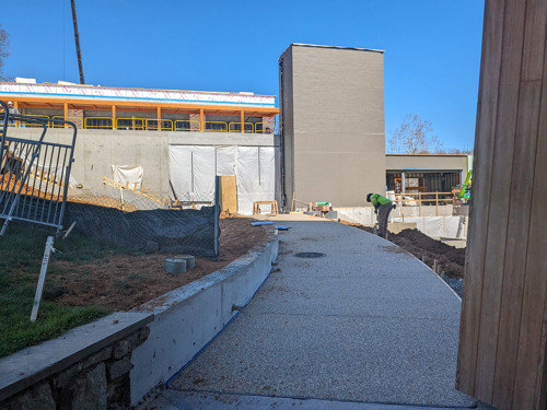 Freshly paved walkway leading to an unfinished building with gray walls and construction materials nearby.