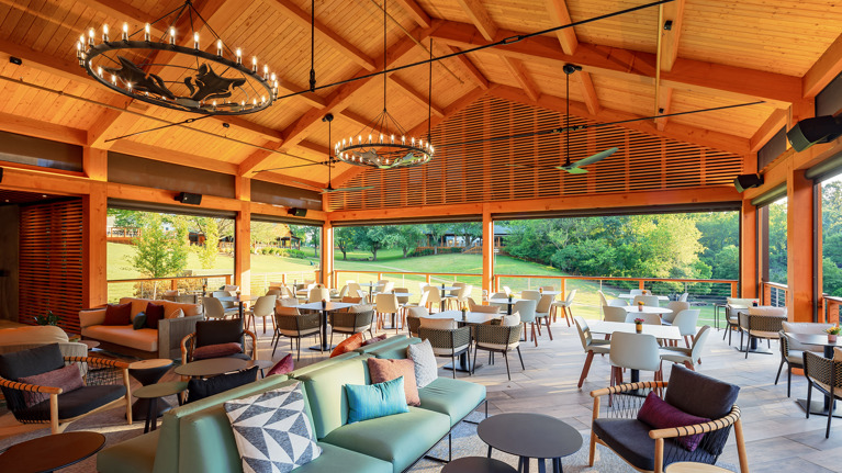 Interior of donor lounge with open-air seating, modern furniture, and large chandeliers under wood-beamed ceiling.