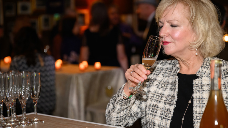 Person smelling champagne at a bar counter with candles and champagne glasses.