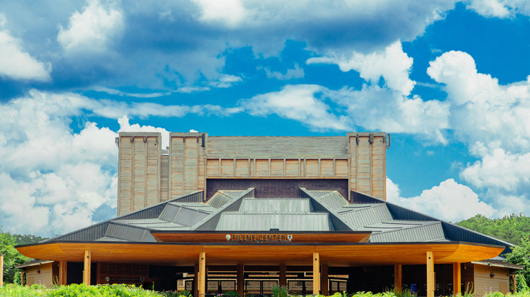 Wide front view of Filene Center main gate with modern wooden roof and building under a bright sky.