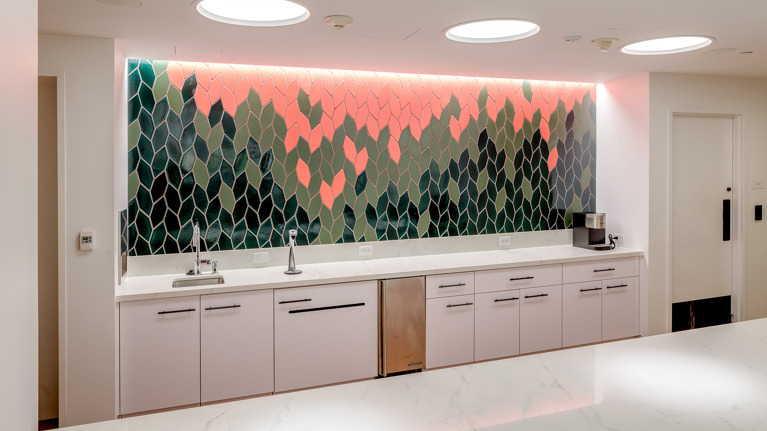 Sleek kitchenette with white counters and cabinets, and a decorative backsplash of green and coral leaf-shaped tiles.