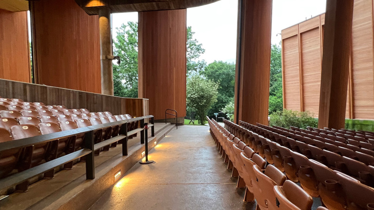 Accessible walkway alongside seating rows with handrails and lighting under tall wooden panels.
