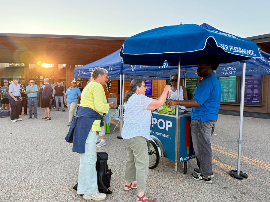 A cart with a blue umbrella, where Kaiser Permanente staff hands a popsicle to a Wolf Trap patron.