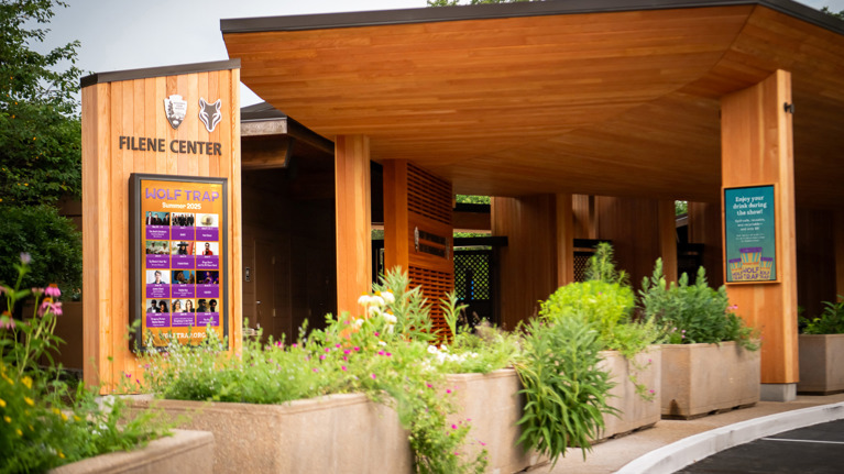 Entrance view featuring Filene Center sign, event poster display, and landscaped planters.